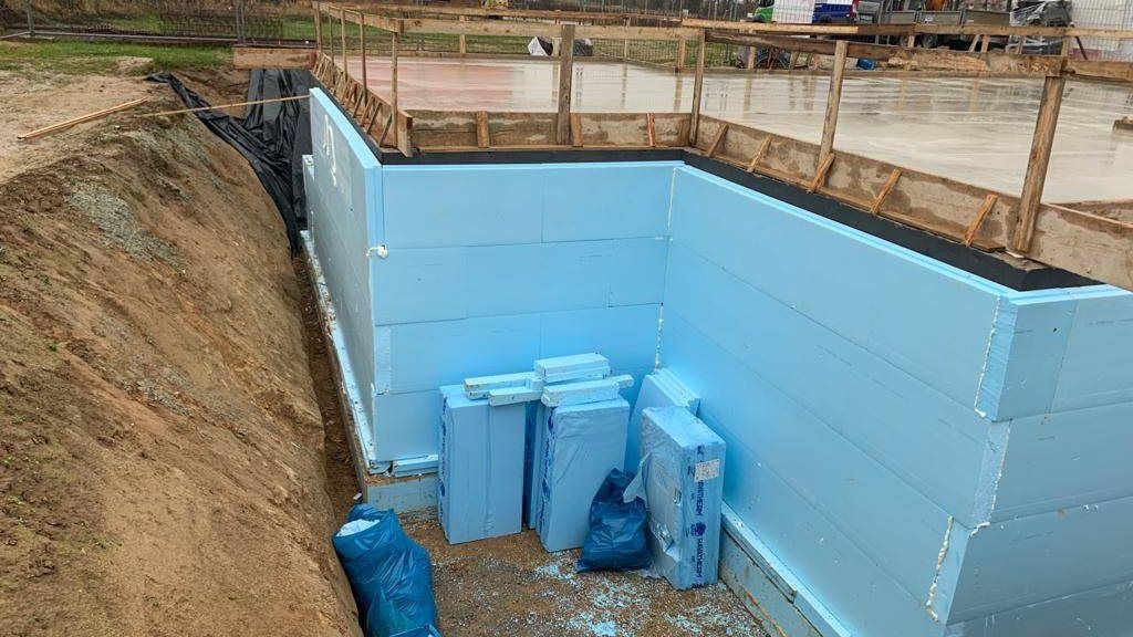 Rechteckige Baugrube mit hellblau gedämmten Wänden und offenem Erdreich an der Böschung