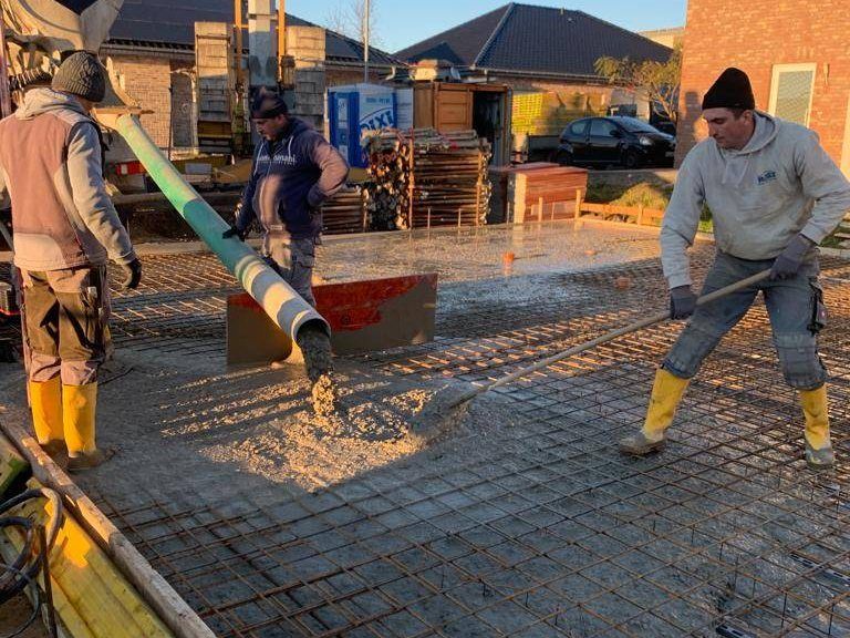 Bauarbeiter verteilen frischen Beton aus dem Pumpenschlauch über der Bewehrung